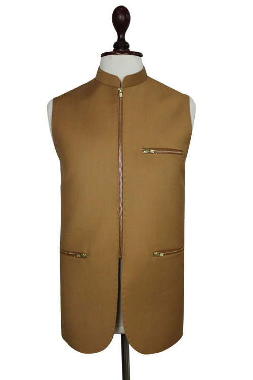 A sleeveless tan waistcoat displayed on a mannequin torso against a plain white background. The vest has a mandarin collar, a front zipper closure, two zippered chest pockets, and two zippered lower pockets, with a thin dark brown trim running down the center front.